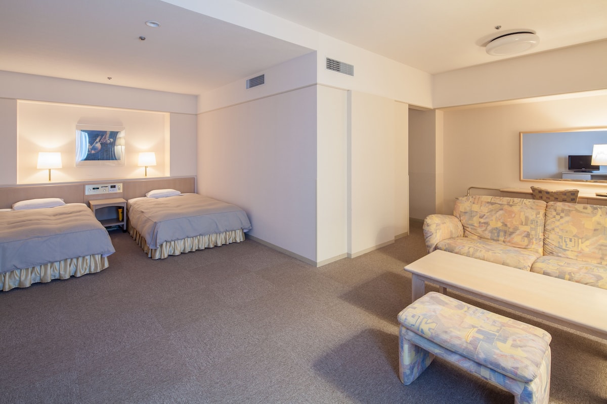 A hotel room with two beds, a sofa, a small table, and a TV.
