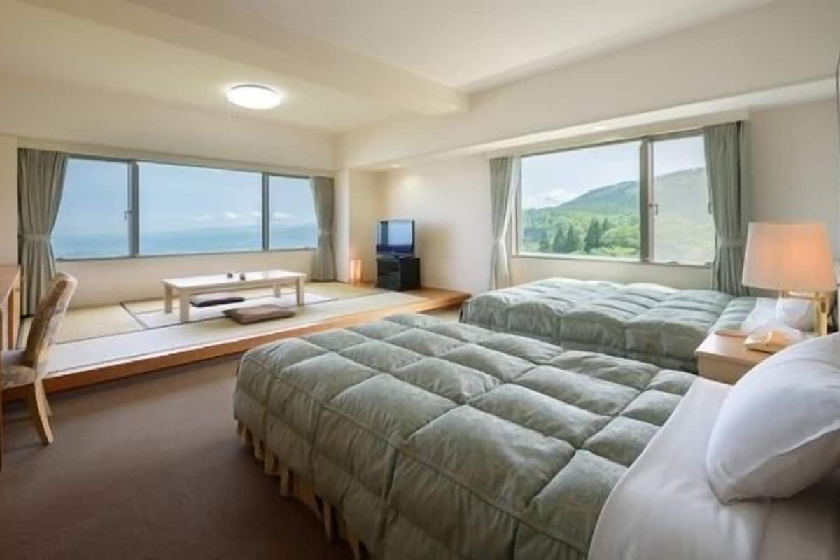 A hotel room with two beds, a desk, a TV, and large windows with a view.