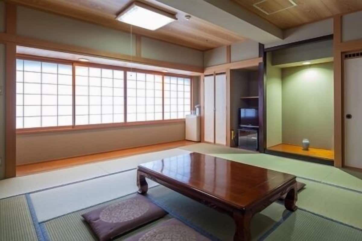 A traditional Japanese room with tatami flooring, a low wooden table, sliding doors, and a television.