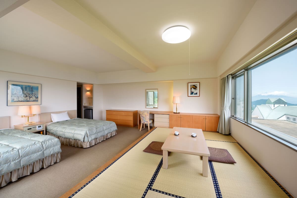 A hotel room with two beds, a desk, a chair, a table, and a large window with a view.