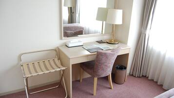 Habitación de hotel con escritorio, silla, lámpara, espejo y ventana con cortinas.