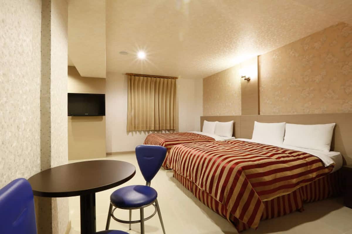 Ein Hotelzimmer mit zwei Betten, einem Fernseher, einem kleinen Tisch und einem Sessel.