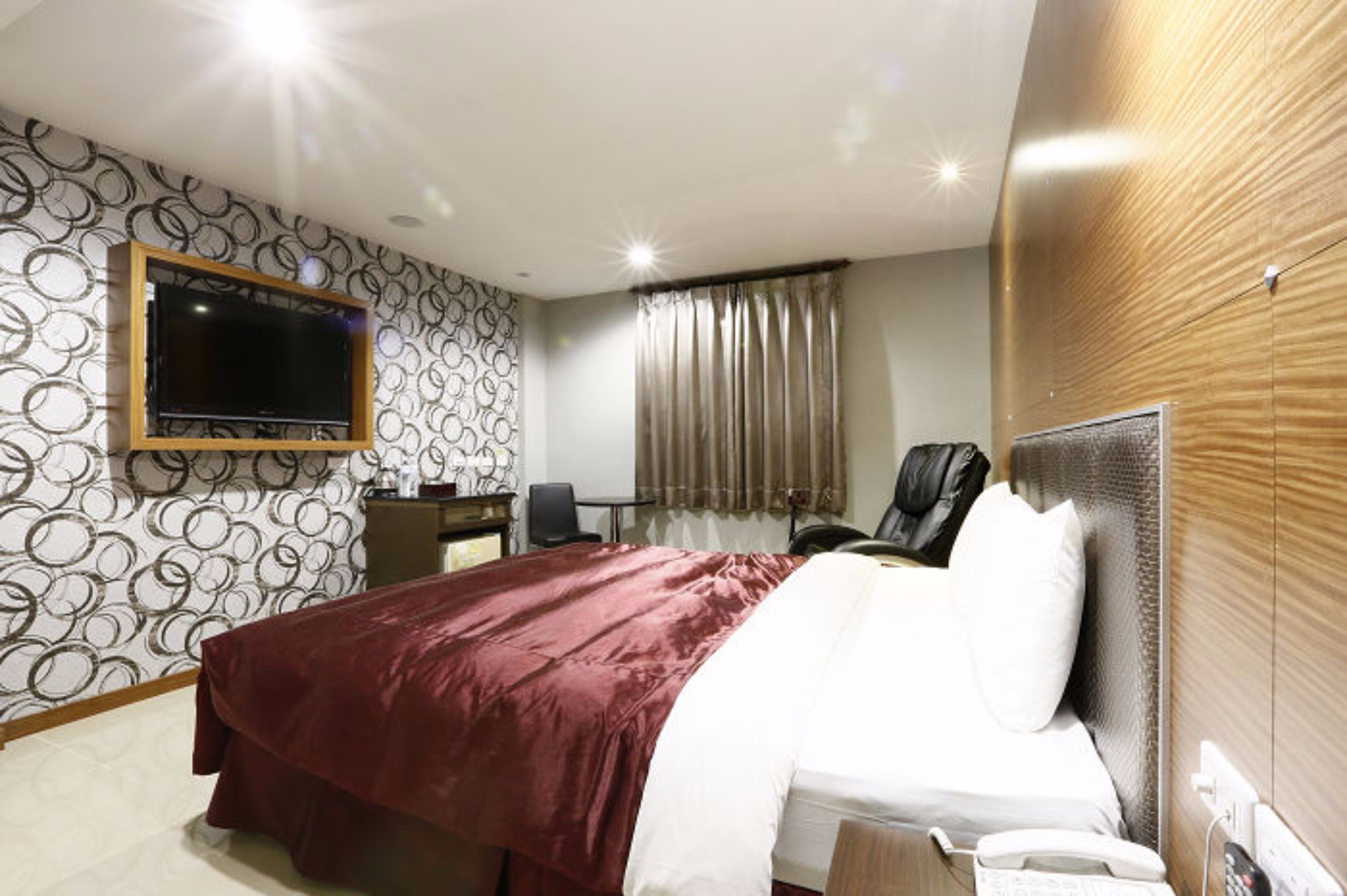 A hotel room with a large bed, a desk with a chair, a television mounted on the wall, and a window with curtains.