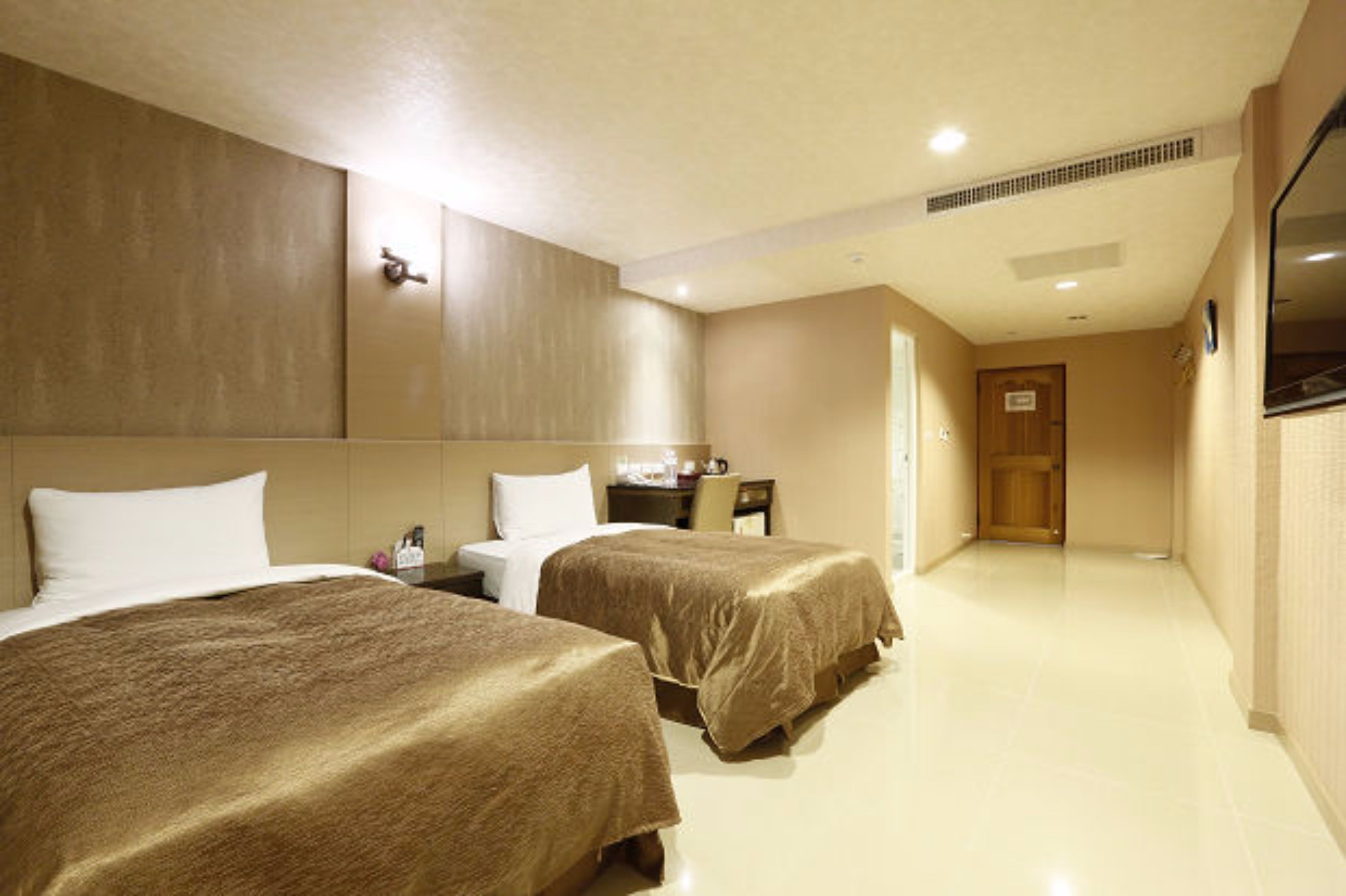 A hotel room with two beds, a desk, and a television.