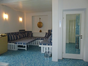 Una stanza con pavimento in piastrelle blu, un divano a righe, un tavolino e una porta che conduce a un bagno con doccia in piastrelle blu.