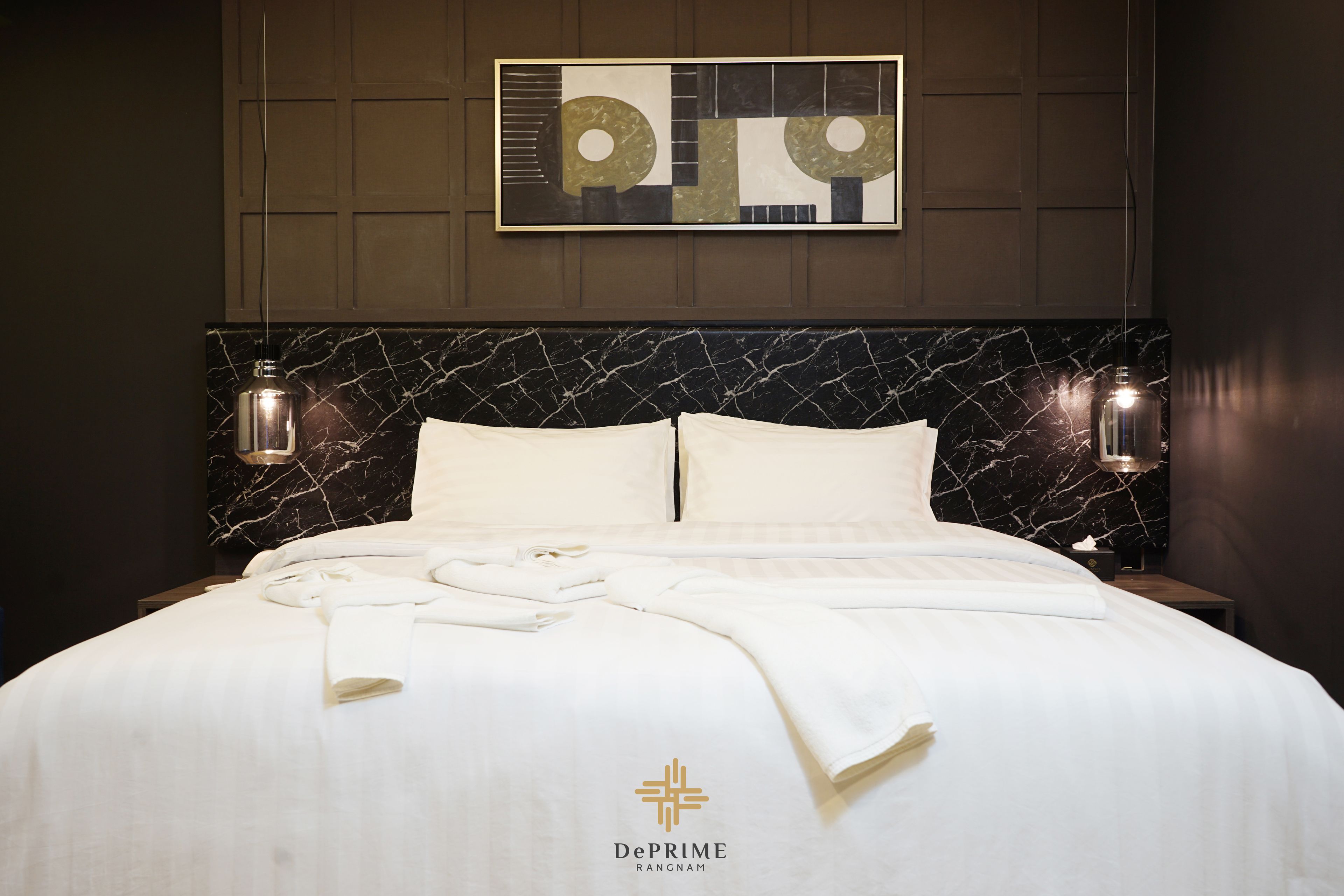 A hotel room with a marble headboard, white bedding, and a DePrime logo on the bed.