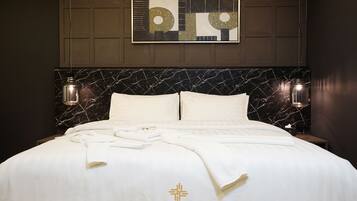 A hotel room with a marble headboard, white bedding, and a DePrime logo on the bed.