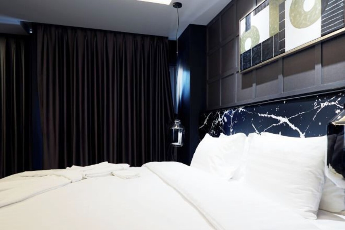 Ein modernes Hotelzimmer mit einem großen Bett, dunklen Vorhängen und einem Marmor-Kopfschild.