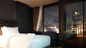 Een moderne hotelkamer met een groot bed, een donkere bank en een groot raam met uitzicht op de stad.