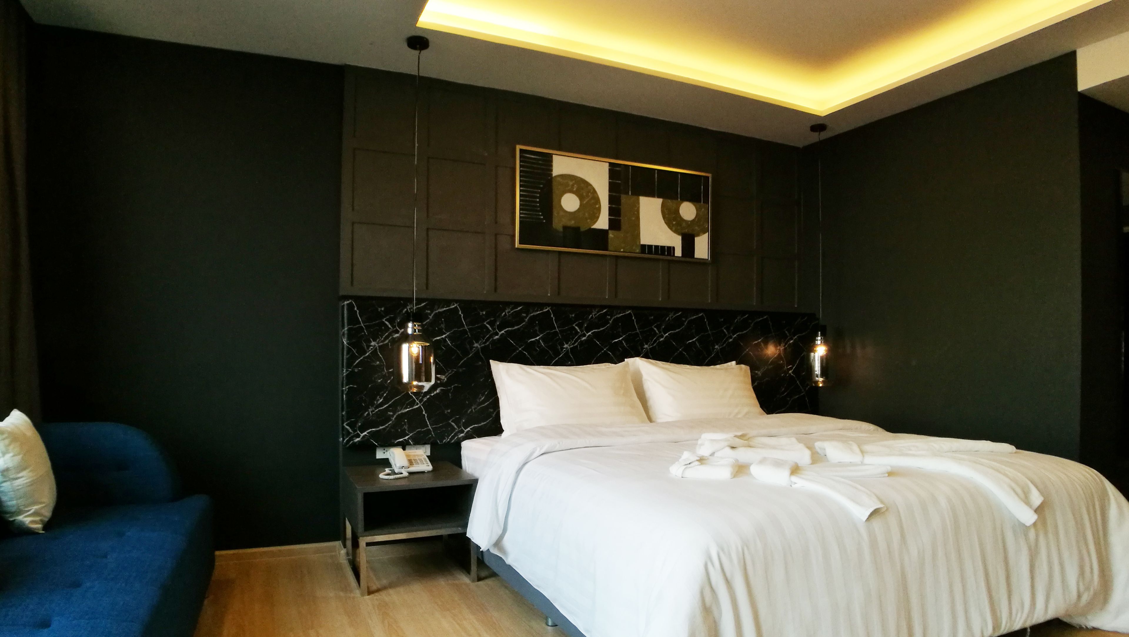 A modern hotel room with a marble headboard, a bedside table with a phone, and a blue sofa.