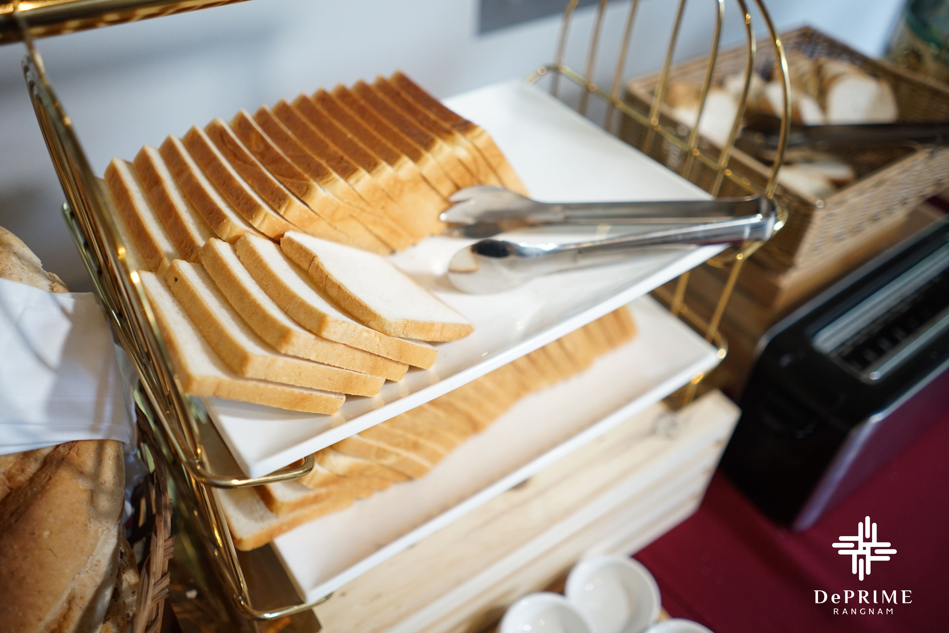 A stack of bread slices on a white plate, with a gold wire rack and a black toaster in the background.