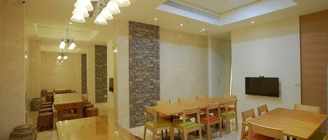 A spacious dining area with a long wooden table and multiple chairs, a stone accent wall, and a television mounted on the wall.