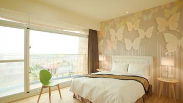 A hotel room with a large bed, a green chair, a balcony with a view, and butterfly wall art.