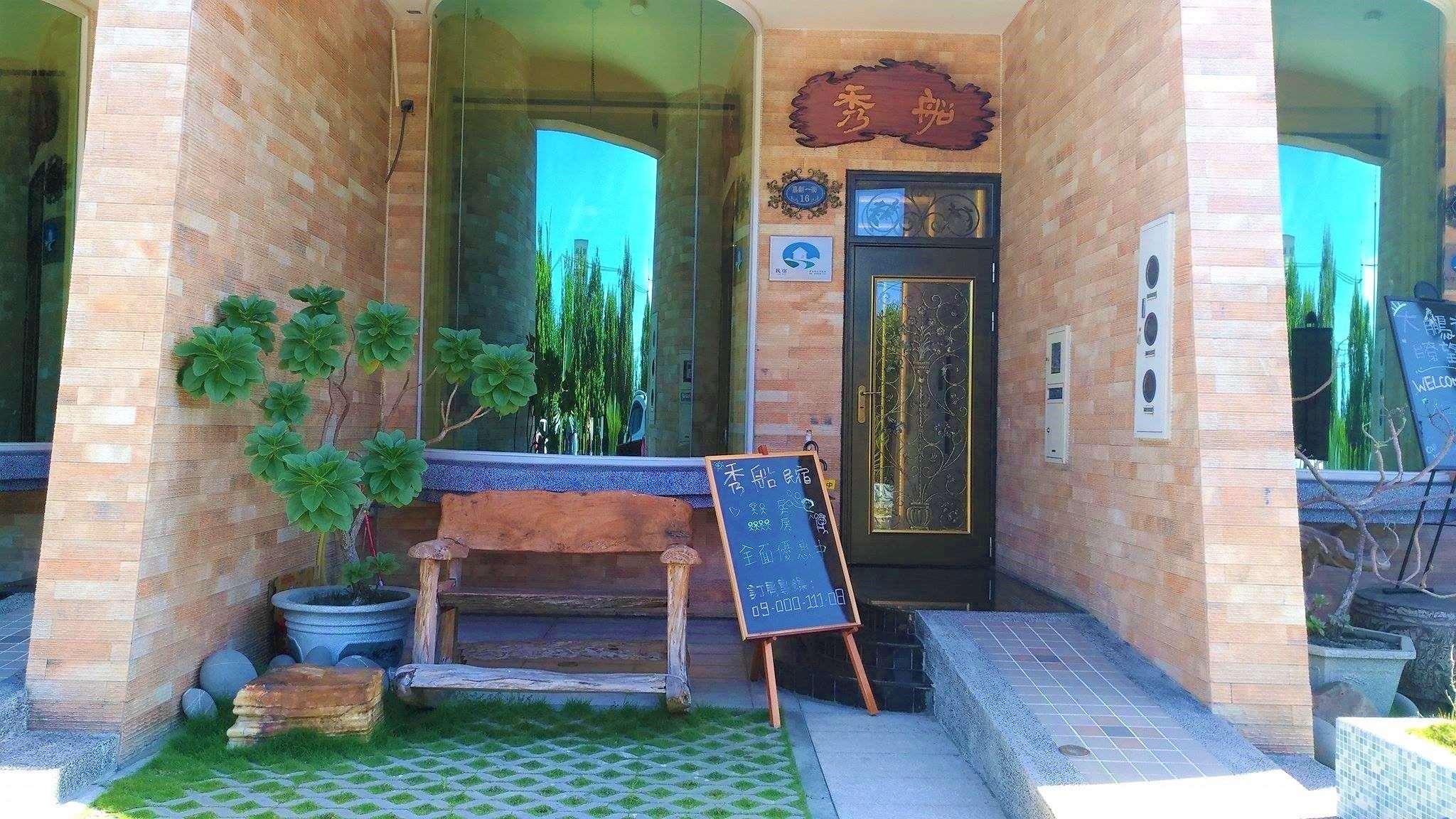 A brick building with a wooden bench and potted plants in front. A chalkboard sign is visible.