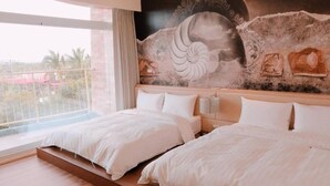 Una habitación de hotel con dos camas, un ventanal con vistas y un mural en la pared.