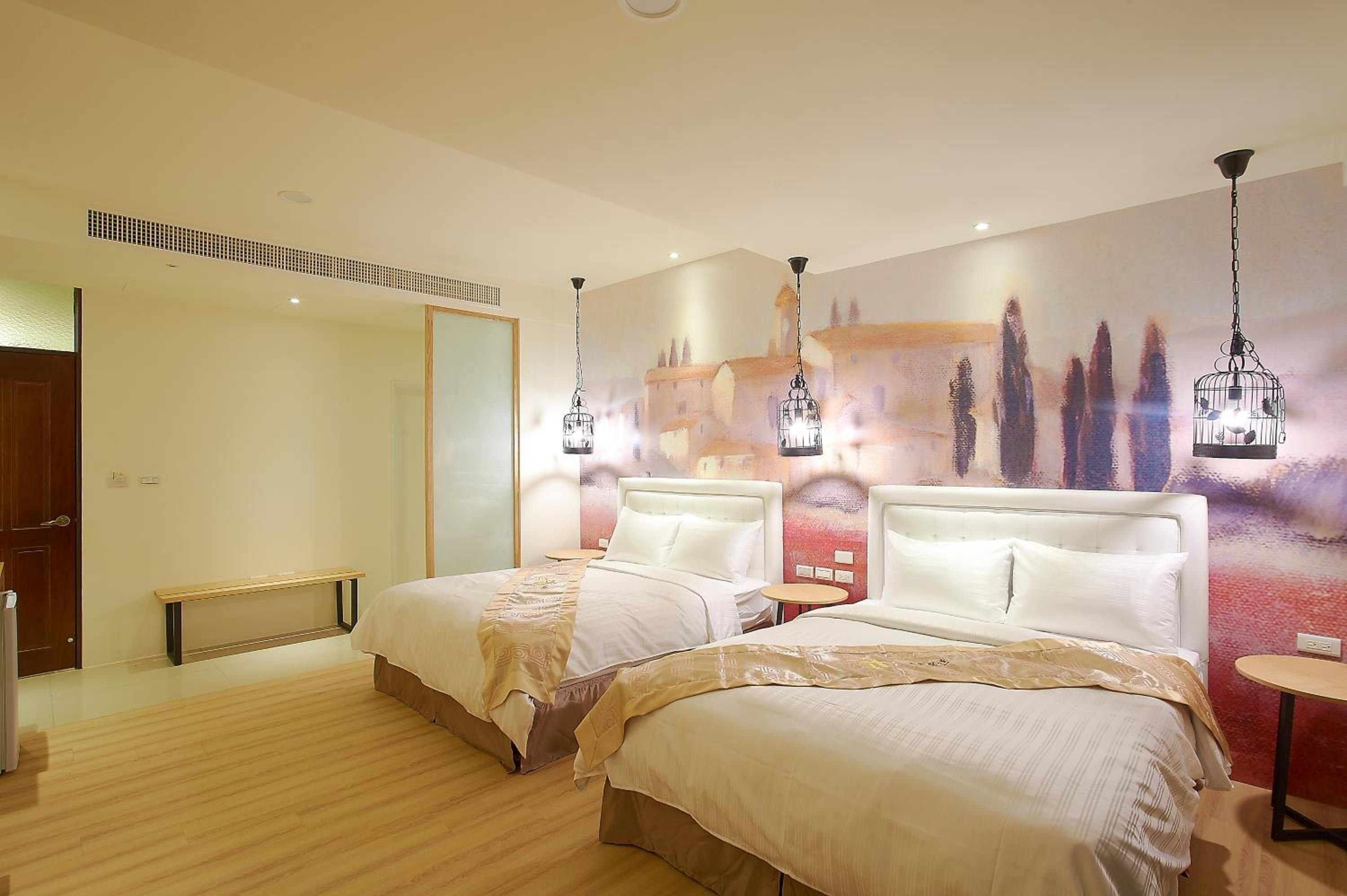 A hotel room with two beds, a bench, a round table, and a wall mural.