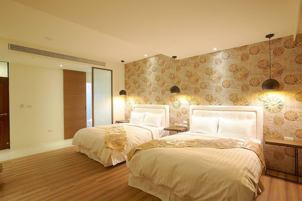 A hotel room with two beds, wooden flooring, and a wall with a clock pattern.