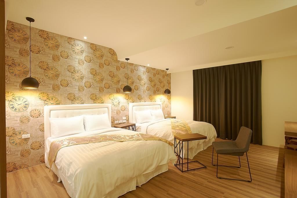 Une chambre d’hôtel avec deux lits, une petite table, une chaise et un mur décoré d’un motif représentant une horloge.