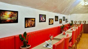 Een restaurant met rode banken en een lange tafel, versierd met schilderijen aan de muur.
