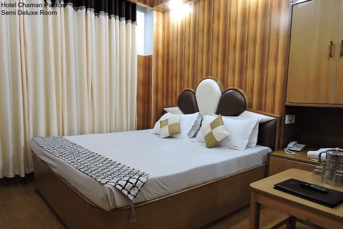 A hotel room with a bed, curtains, a wooden headboard, a bedside table with a phone and a remote control, and a wooden wardrobe.