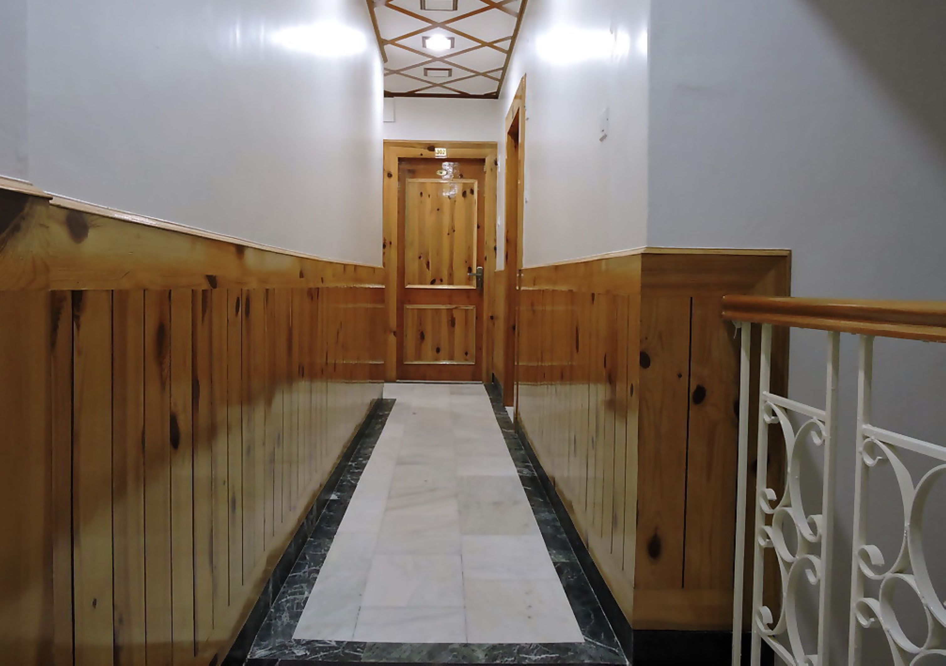 A hallway with wooden paneling, a marble floor, and a wooden door at the end.
