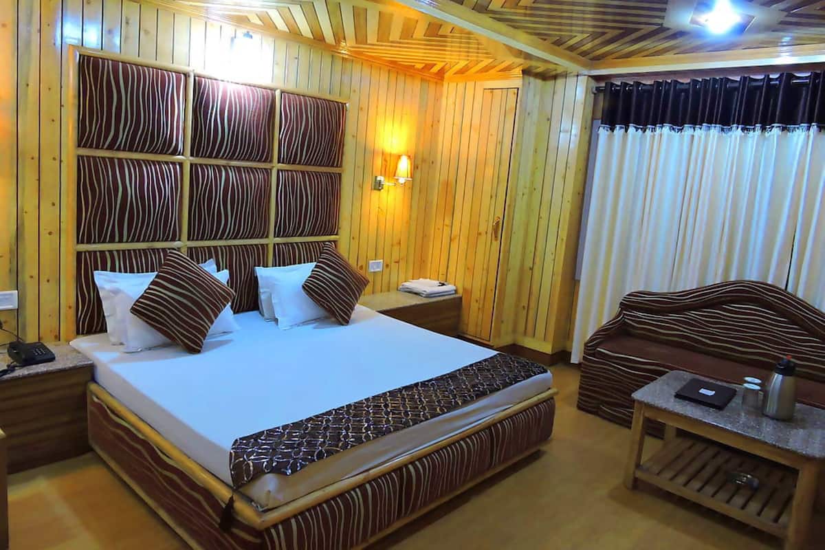 A hotel room with a large bed, wooden panel walls, a nightstand with a phone, and a small table with a lamp.