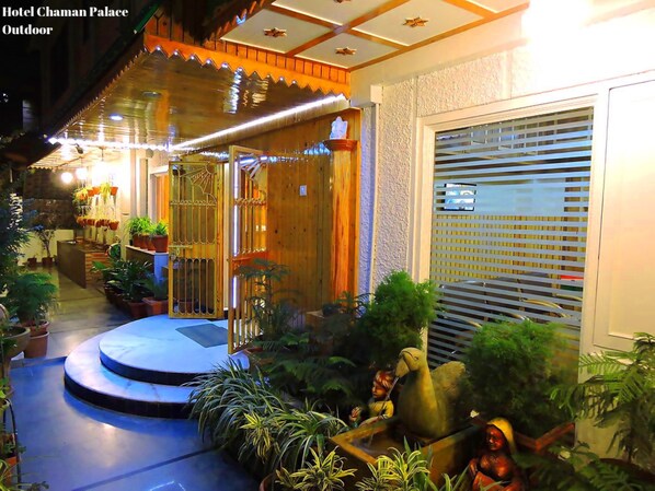 Fachada de hotel de madera, entrada con portón y diversos maceteros.