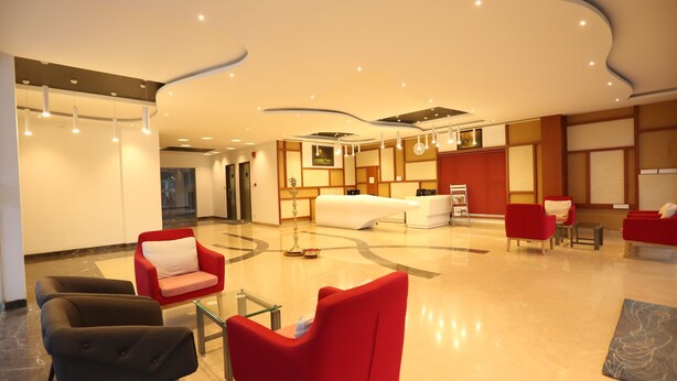A spacious lobby with a modern design, featuring a reception desk, seating area with red and black chairs, and a large bed in the background. - Hotel Jump In & Out (Coimbatore)