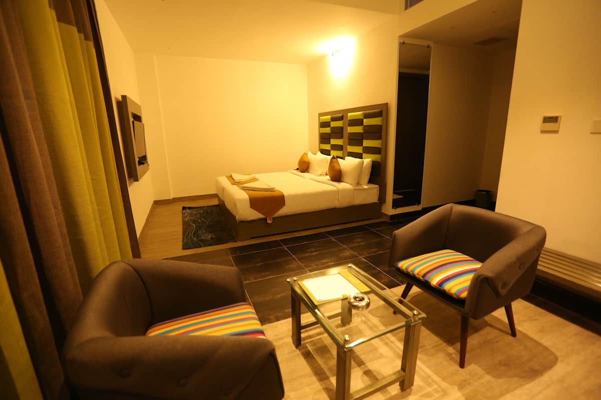 A hotel room with a bed, two armchairs, a glass coffee table, and a small table with a lamp.