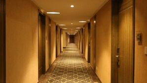 A long, narrow hotel corridor with doors on both sides, a patterned carpet, and overhead lighting. - Hotel Jump In & Out (Coimbatore)