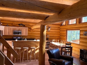 A log cabin interior with a kitchen, dining area, and bar stools.