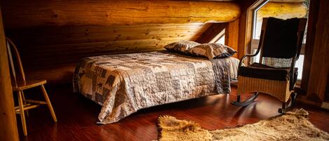 A cozy cabin interior with a wooden bed, a rocking chair, and a large fur rug.