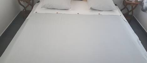 A neatly made bed with white linens and two pillows, flanked by wooden nightstands with lamps.