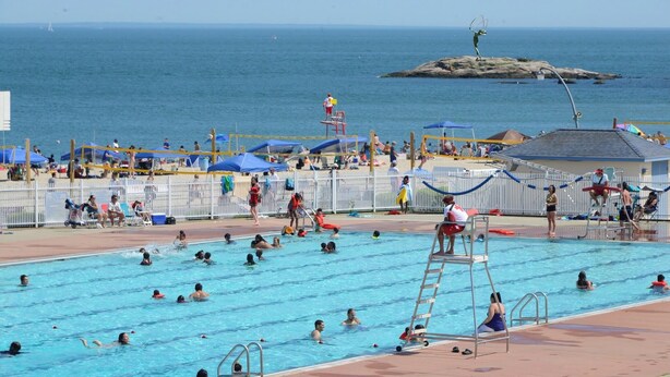 Ein Schwimmbecken mit mehreren Bahnen, einem Rettungsschwimmturm und Blick auf den Ozean.