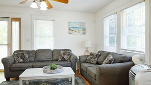 Ein Wohnzimmer mit zwei grauen Sofas, einem weißen Couchtisch, einem gemusterten Teppich und einem Deckenventilator.