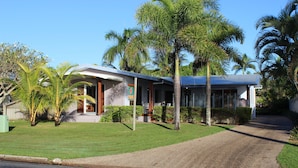 A modern house with a paved driveway, surrounded by palm trees and well-maintained lawns. - Banfields Retreat (Wongaling Beach)