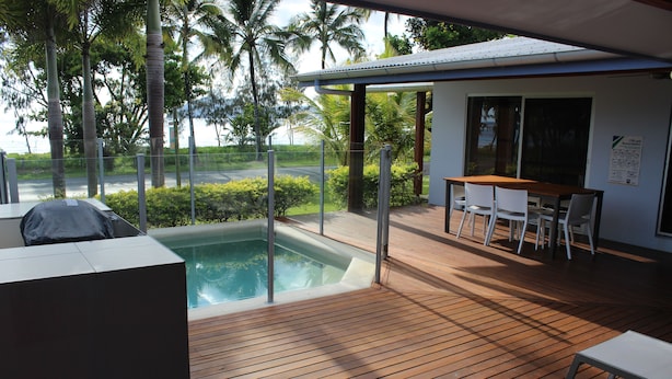 A wooden deck with a hot tub, a covered seating area, and a view of palm trees. - Banfields Retreat (Wongaling Beach)