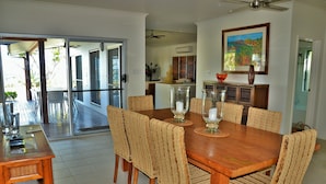 A dining area with a wooden table and woven chairs, a glass-top coffee table, and a view of the outdoor patio. - Banfields Retreat (Wongaling Beach)