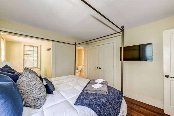 Un dormitorio con una cama con dosel, un televisor montado en la pared y una puerta que da a otra habitación.