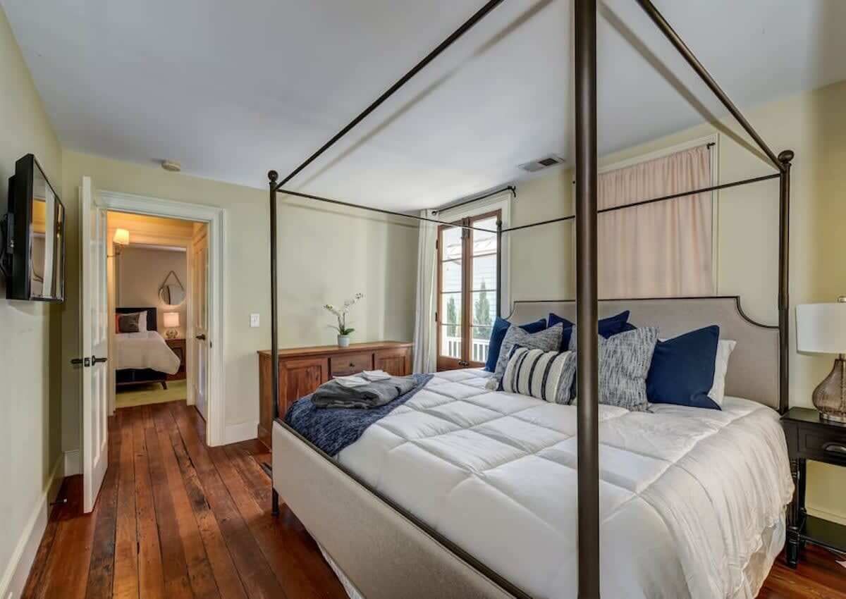 Una cama con dosel en un dormitorio con piso de madera, una mesita de noche y un ventanal con cortinas.