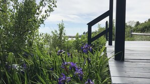 Een houten terras met een leuning, omgeven door weelderige begroeiing en paarse bloemen.