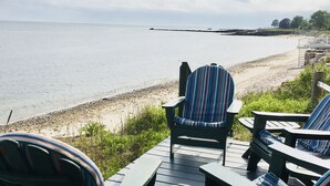 Een terras met Adirondack stoelen en een tafel, met uitzicht op het strand.