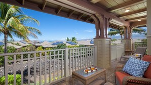 A covered outdoor area with wicker furniture, a table with a drink, and a view of a beach with houses and palm trees. - Mauna Lani Private beach access, 2026 Hilton Waikoloa Pool pass included! (Waimea)