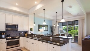 A modern kitchen with white cabinets, a granite countertop, stainless steel appliances, pendant lighting, and a view of the outdoors through large windows. - Mauna Lani Private beach access, 2026 Hilton Waikoloa Pool pass included! (Waimea)