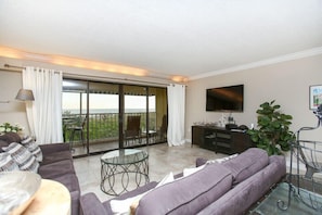Relax in the living room with a sofa, flat-screen TV, and a balcony offering a view of the surrounding landscape.