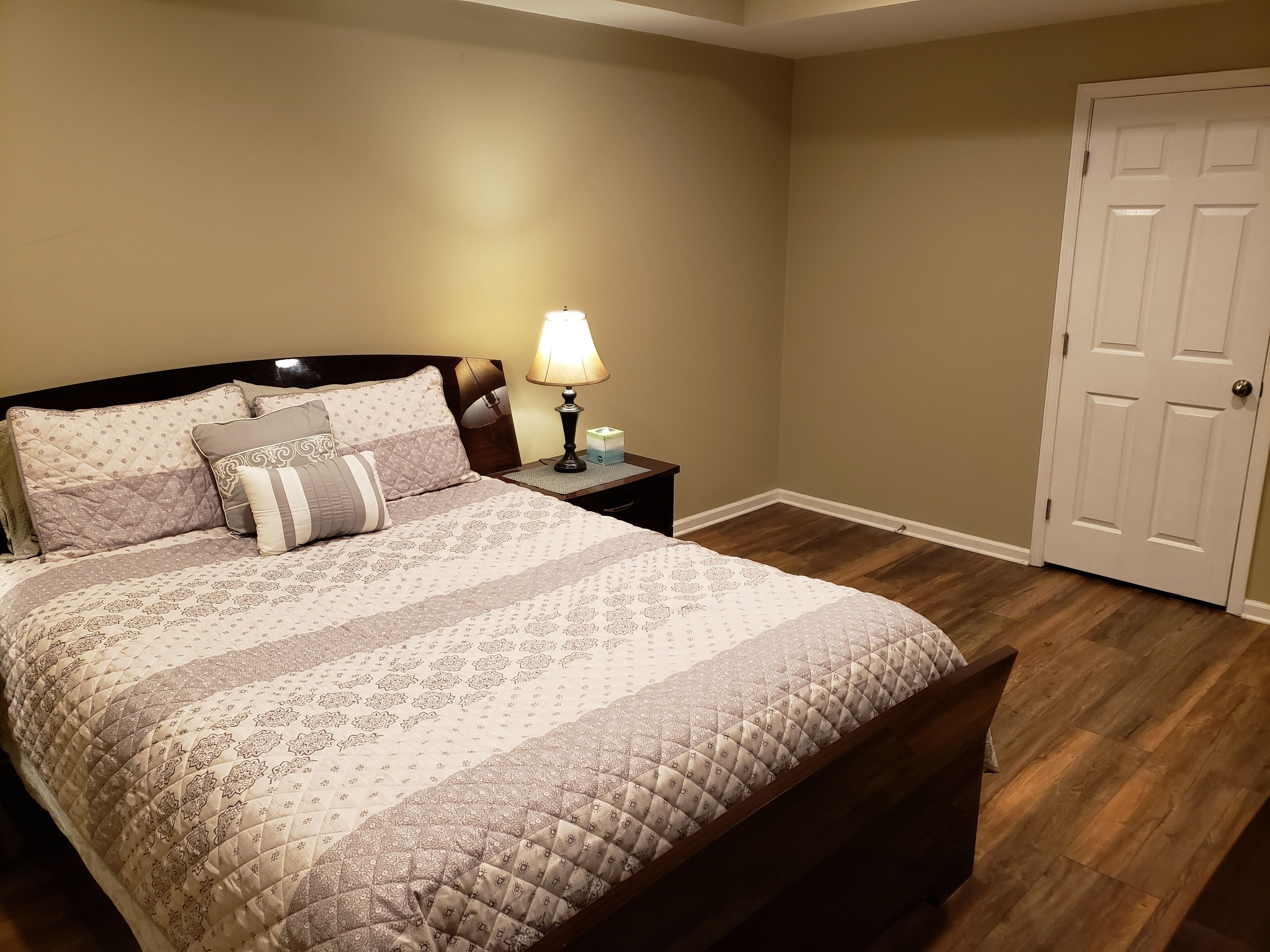 A bedroom with a bed, nightstand, lamp, and a door.