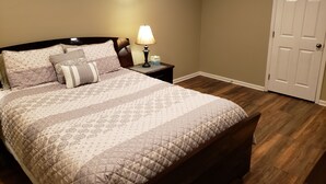 Quarto com cama, mesa de cabeceira, abajur e porta.