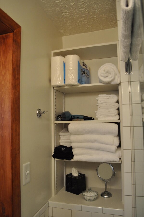 A bathroom with a shelf holding towels, toiletries, and a hairdryer.