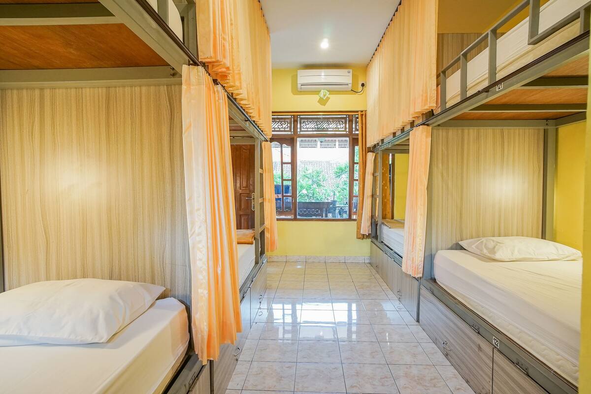 A dormitory room with bunk beds, a tiled floor, and a window with a view of greenery.