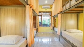 A dormitory room with bunk beds, a tiled floor, and a window with a view of greenery.